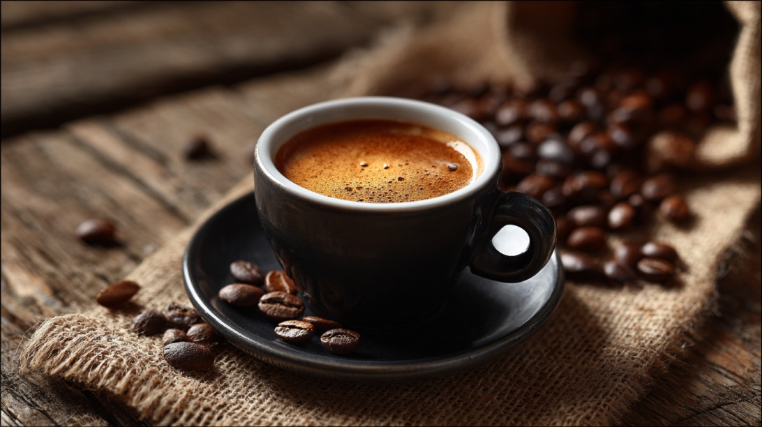 Šoljica espreso kafe na drvenoj podlozi okružena zrnima kafe