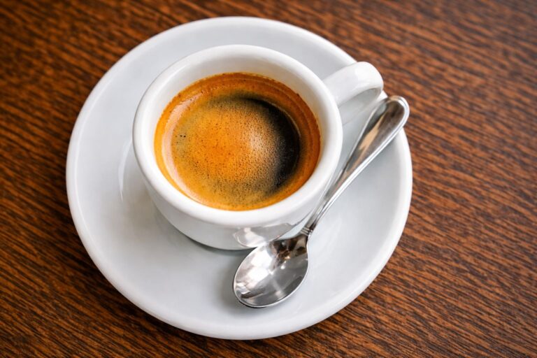 Espreso u beloj šoljici snimljen odozgo sa jasno vidljivom kremom i kašičicom na tacni